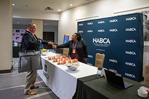 Hotel conference lobby registration area with a long table, where male attendee receives name badge from event representative.