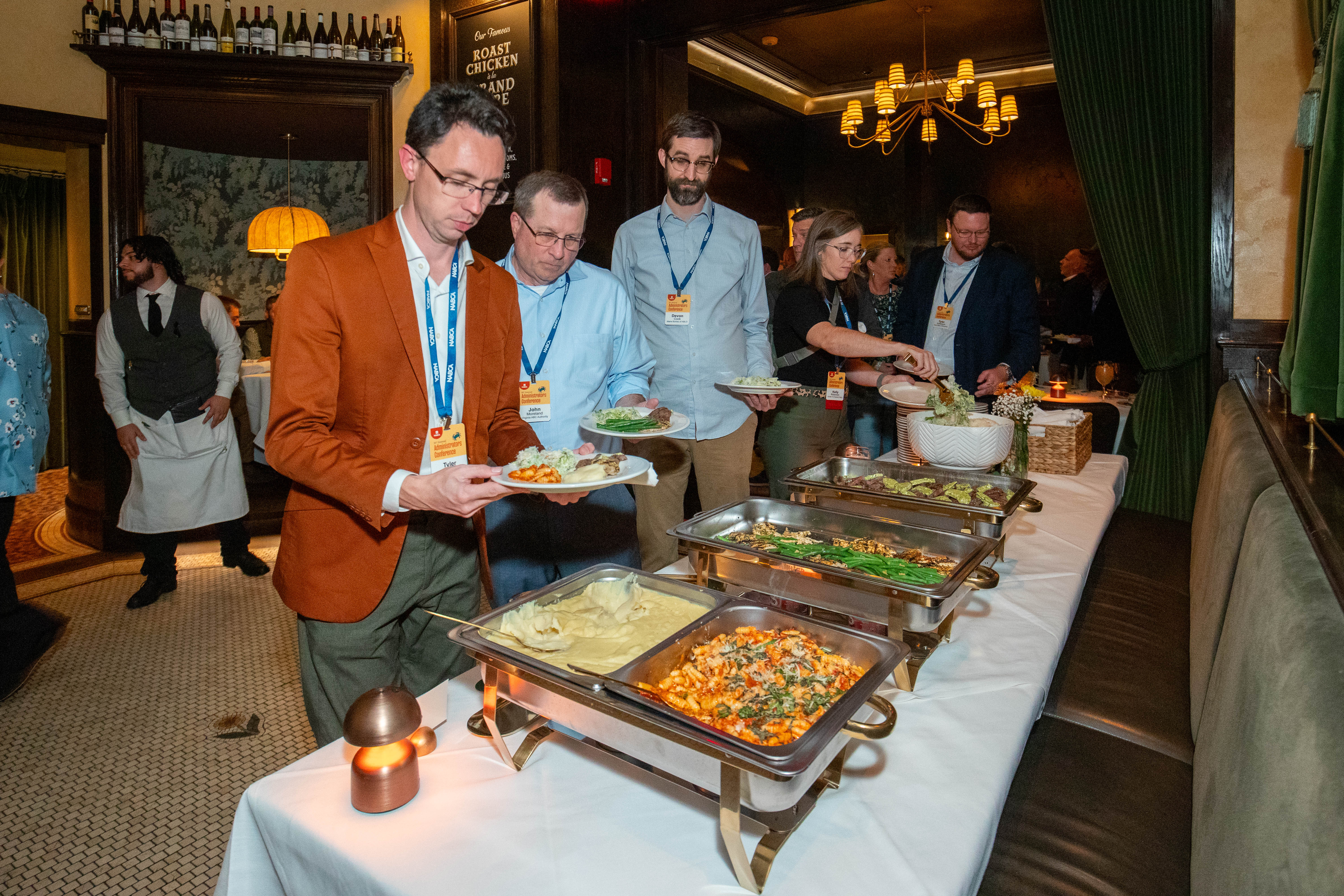 Foreground shows a buffet table with food and people serving themselves. Background shows restaurant staff. 