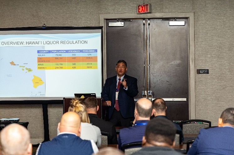 A man standing beside a projection screen talking to a group of seated people